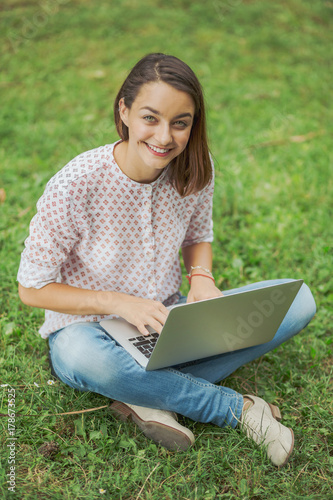 Young woman with laptop sitting on green grass © arthurhidden