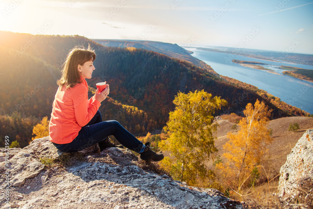 the girl is drinking tea on top of the mountain, holding a mug in her hands