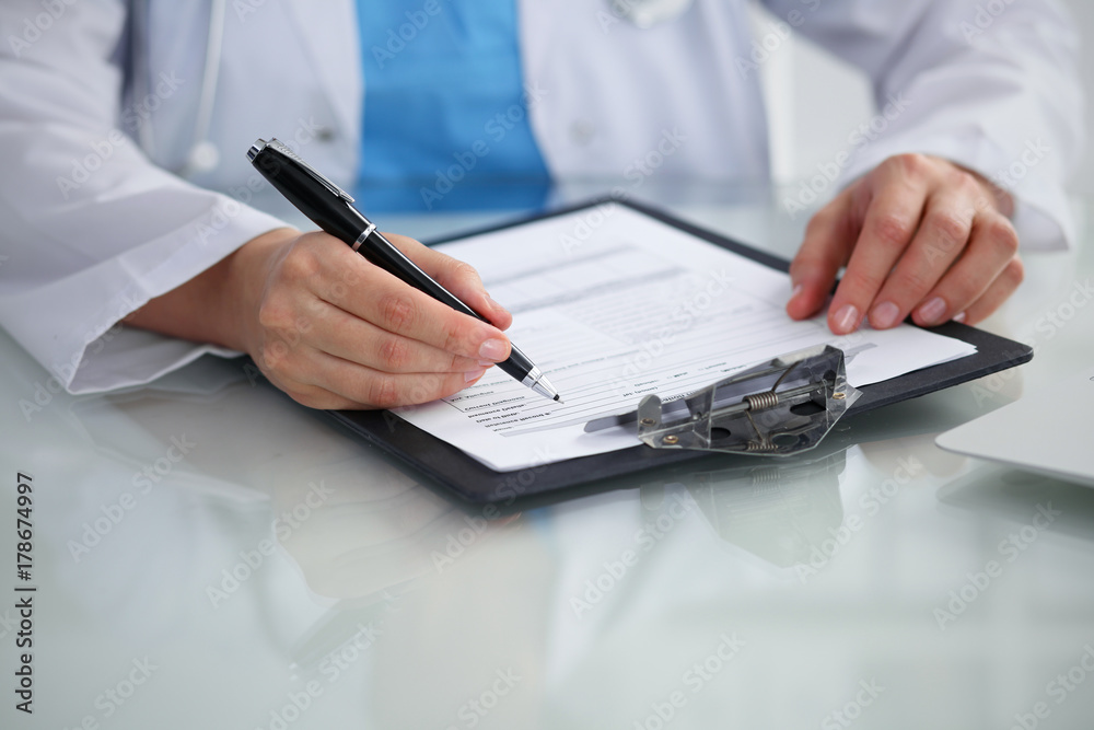 Doctor woman filling up medical form while sitting at the table, close-up of hands Doctor woman filling up medical form while sitting at the table, close-up of hands