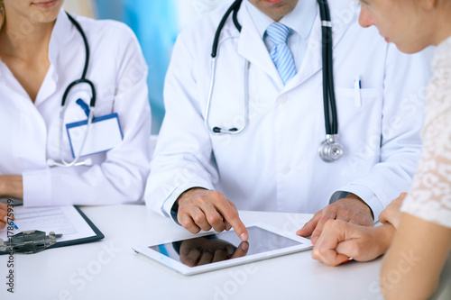 Doctor and patient talking while sitting at the desk in office. Physician pointing into touch pad computer or tablet. Medicine and health care concept