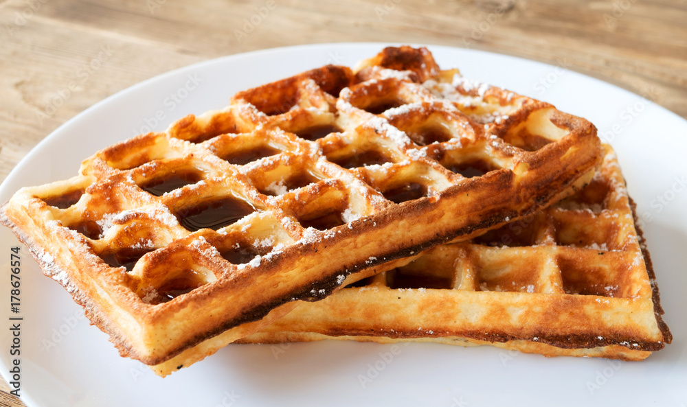 Sweet waffles with maple syrup topping on white plate. Tasty morning dessert