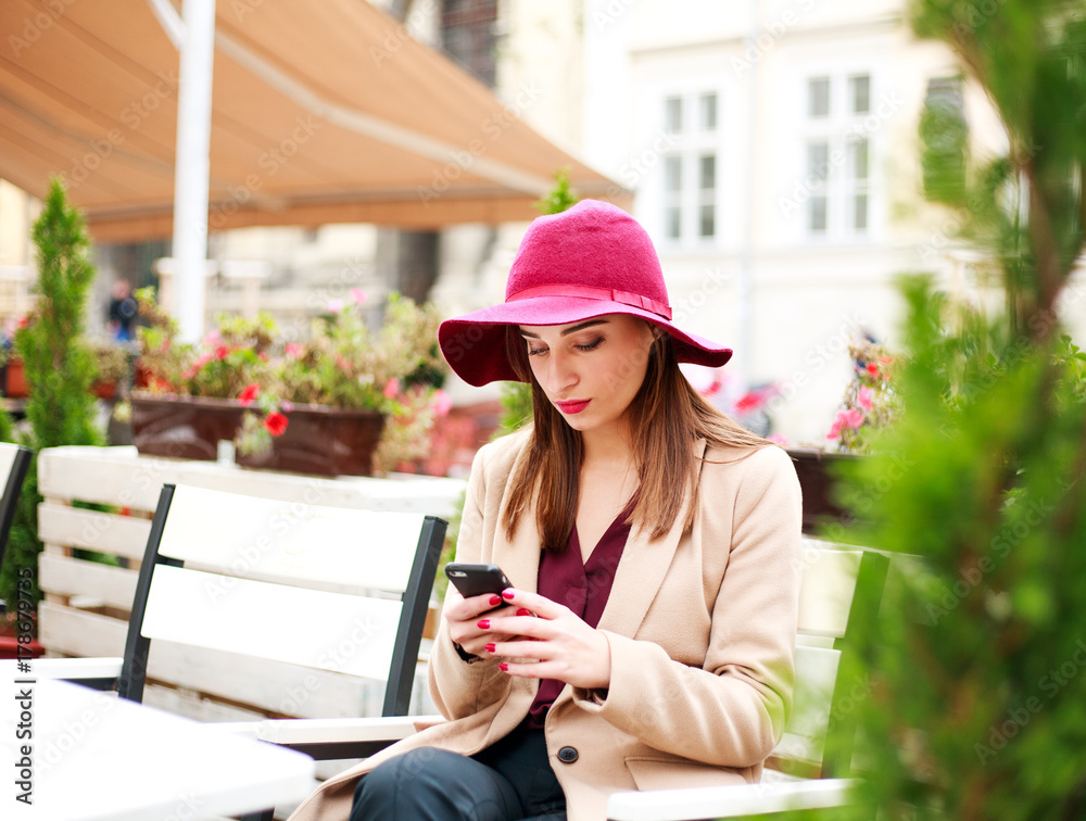 Elegant young woman at street cafe with phone on town background
