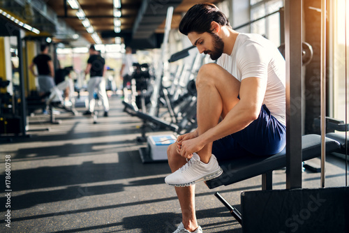 Handsome bearded man ties up his shoelaces on sneakers at the gym before exercises.