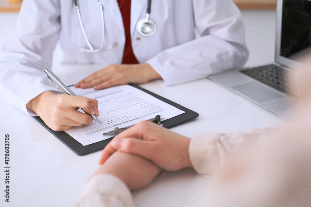 Close up of a female doctor filling up an application form while consulting patient Close up of a female doctor filling up an application form while consulting patient