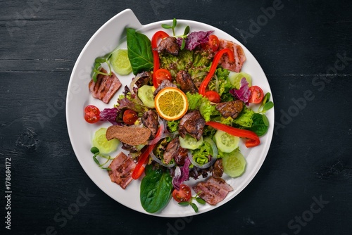 Salad with bacon and chicken liver. On a wooden surface. Top view. Free space for your text.