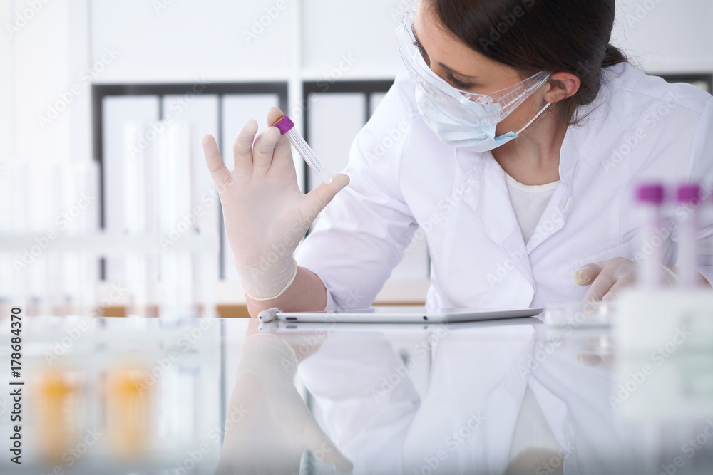 Close-up of professional female scientist in protective eyeglasses making experiment with reagents in laboratory. Medicine and research concept Close-up of professional female scientist in protective eyeglasses making experiment with reagents in laboratory. Medicine and research concept