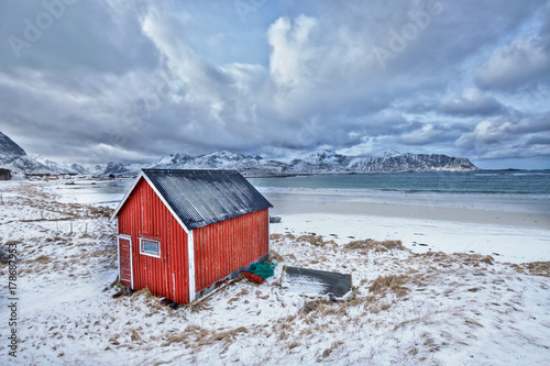 Red rorbu house shed on beach of fjord, Norway