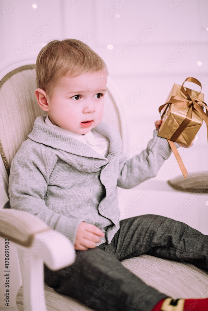 Cheerful little baby boy playing with gifts and presents near Christmas tree, gold and beige pastel c Cheerful little baby boy playing with gifts and presents near Christmas tree, gold and beige pastel c