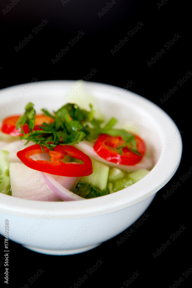 Thai cuisine, vinegar with cucumber, onion, chili and coriander in white bowl on black background.