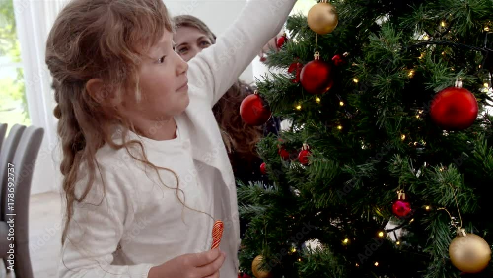 Cute girl and her mother decorating Christmas tree. Young family preparing for Christmas at home. Cute girl and her mother decorating Christmas tree. Young family preparing for Christmas at home.
