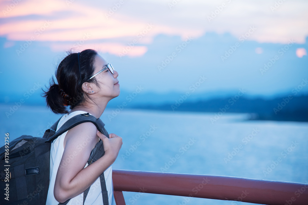 Asian backpacker woman breathing fresh air on sea and sunset sky background.