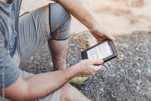 man reading eBook outdoors on a beach, leisure at hiking trip