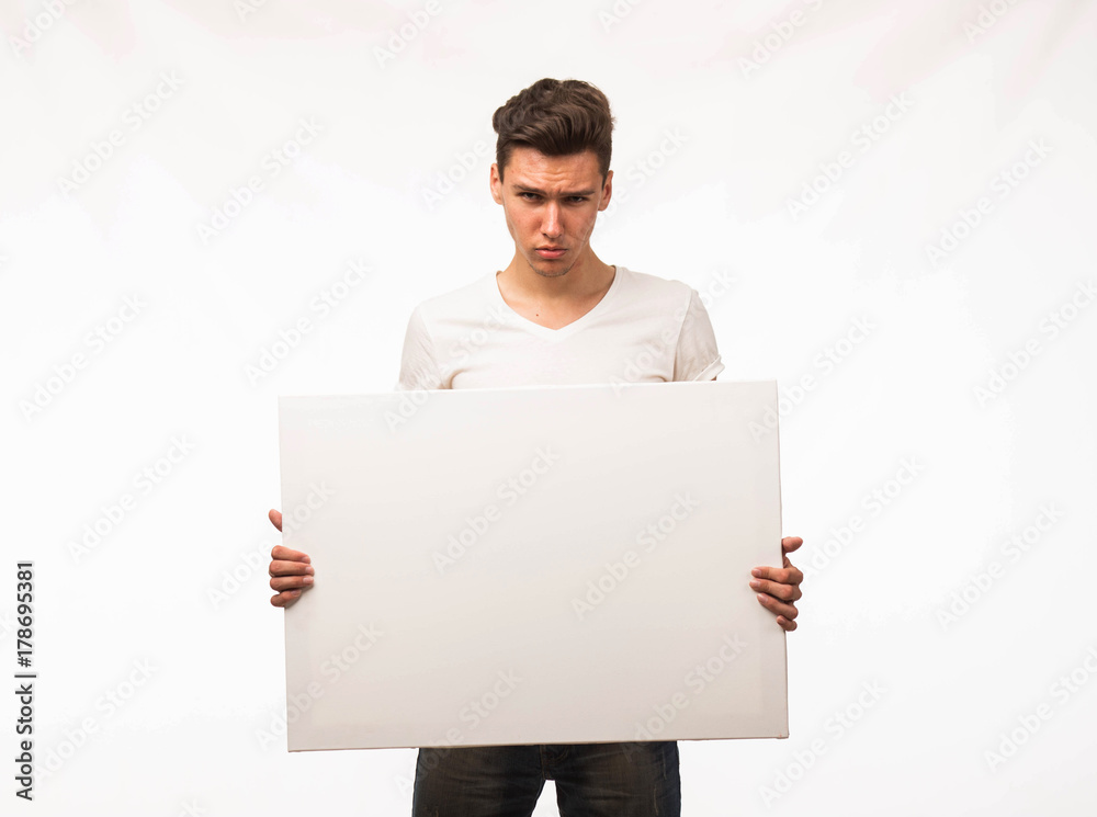 Young serious man portrait of a confident businessman showing presentation, pointing paper placard gray background. Ideal for banners, registration forms, presentation, landings, presenting concept. Young serious man portrait of a confident businessman showing presentation, pointing paper placard gray background. Ideal for banners, registration forms, presentation, landings, presenting concept.