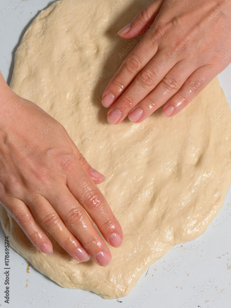 Hands knead the dough for making pizza.