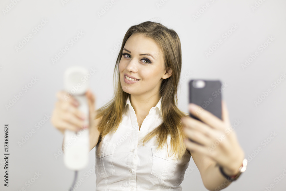 The beautiful girl holds two phones. Beautiful girl in a business suit on a white background with two phones. Different emotions on the face when talking on the phone The beautiful girl holds two phones. Beautiful girl in a business suit on a white background with two phones. Different emotions on the face when talking on the phone