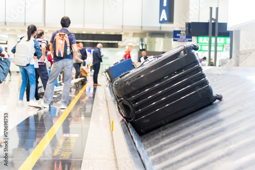Suitcase on luggage conveyor belt at baggage claim at airport. Lines of people waiting for their baggage