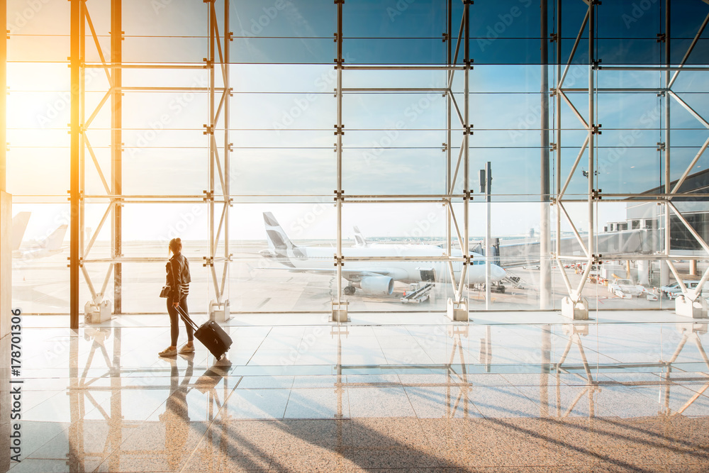 View on the aiport window with woman walking with suitcase at the departure hall during the sunset. Wide angle view with copy space View on the aiport window with woman walking with suitcase at the departure hall during the sunset. Wide angle view with copy space