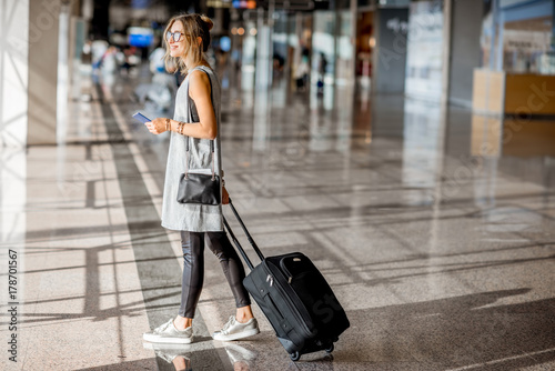 Young woman in grey dress walking with suitcase at the departure hall of the airport waiting for the flight