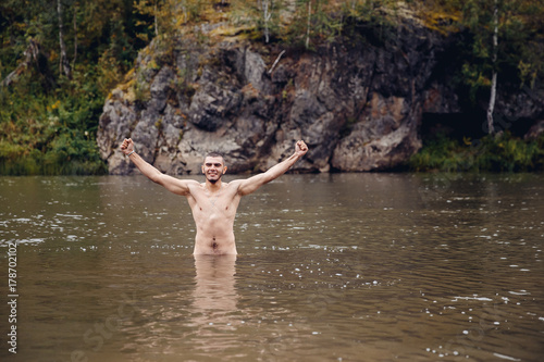 man bathes in a cold river against the background of mountains and rocks