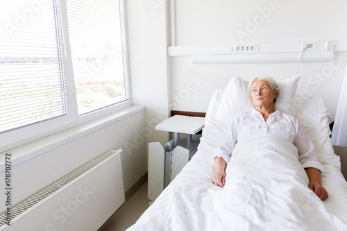 sad senior woman lying on bed at hospital ward