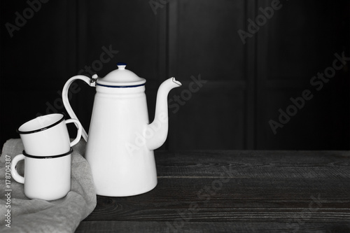 Metal teapot and mugs on the black wooden table
