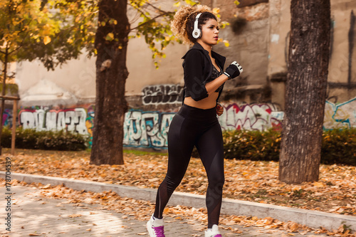 Beautiful jogger portrait in urban autumnal park, wearing headphones and sporty clothes