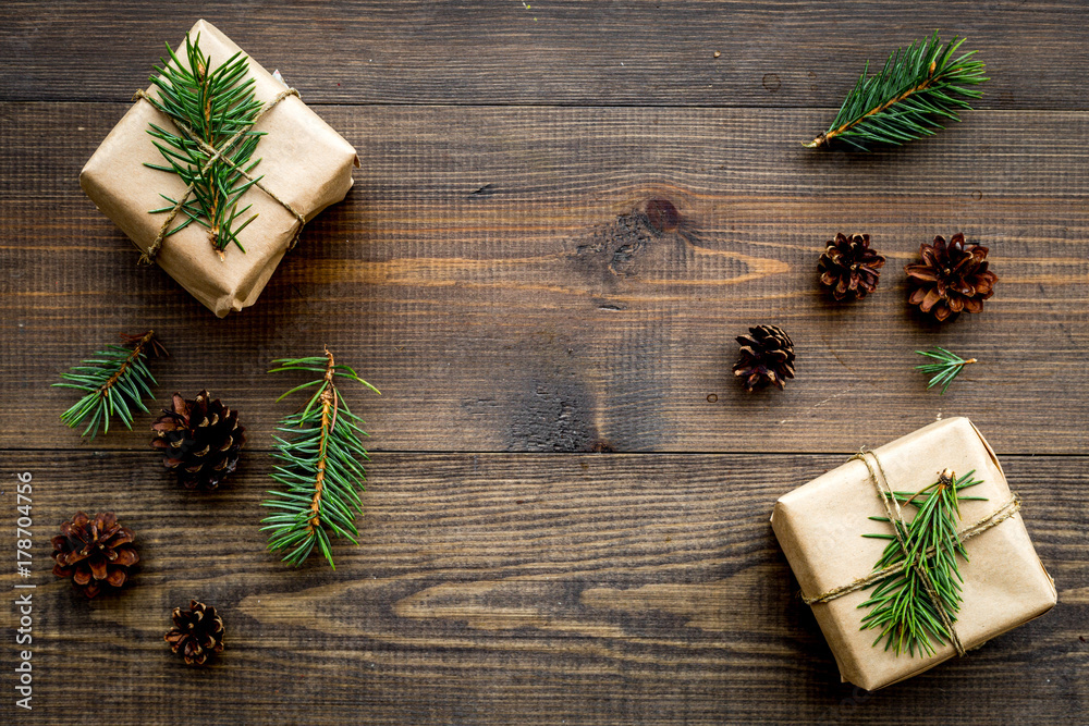 Gifts for new year wrapped in craft paper near spruce branches and cones on wooden background top view pattern copyspace Gifts for new year wrapped in craft paper near spruce branches and cones on wooden background top view pattern copyspace