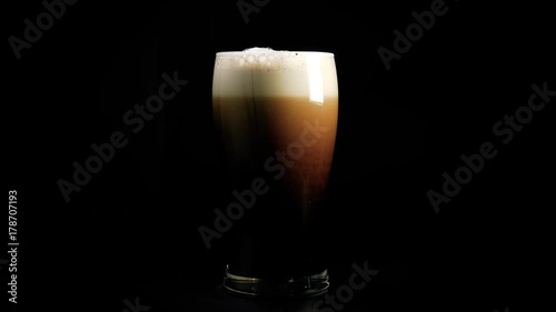 A pint of dark beer foam beautifully against black background photo