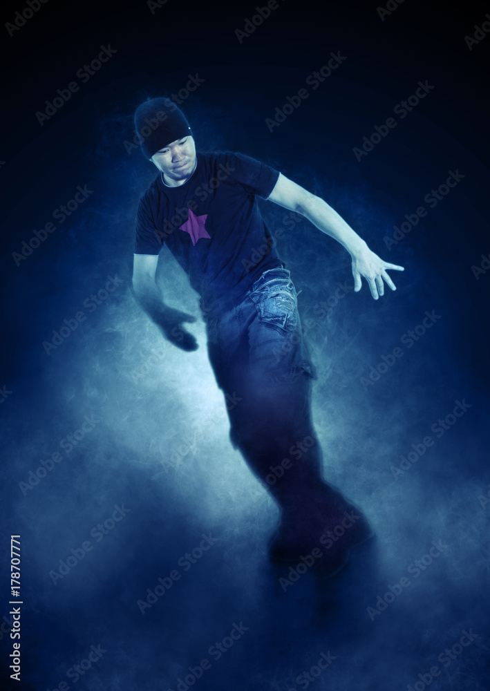Fototapeta premium Young man break dancing on dark smoke background