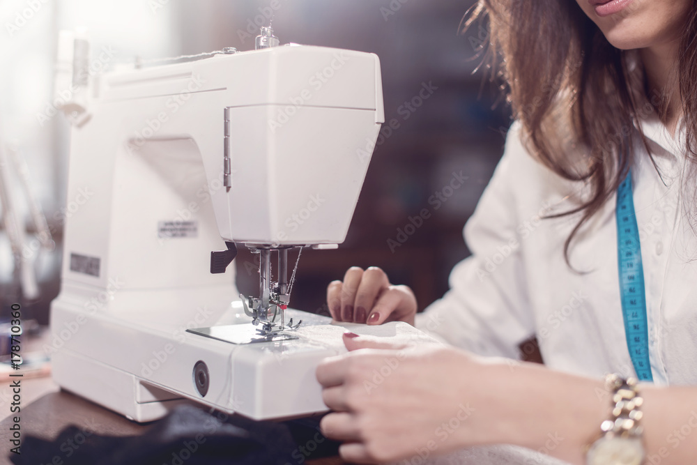 Cropped image of female tailor stitching fine lace with sewing machine sitting in dressmaking studio