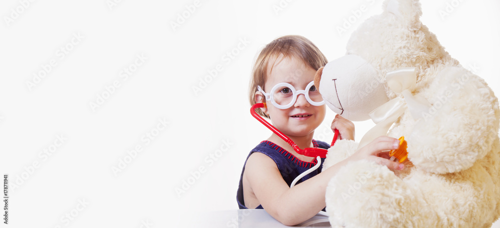Girl playing doctor and treats teddy bear (Health, medicine, hospital, veterinary medicine concept) Girl playing doctor and treats teddy bear (Health, medicine, hospital, veterinary medicine concept)