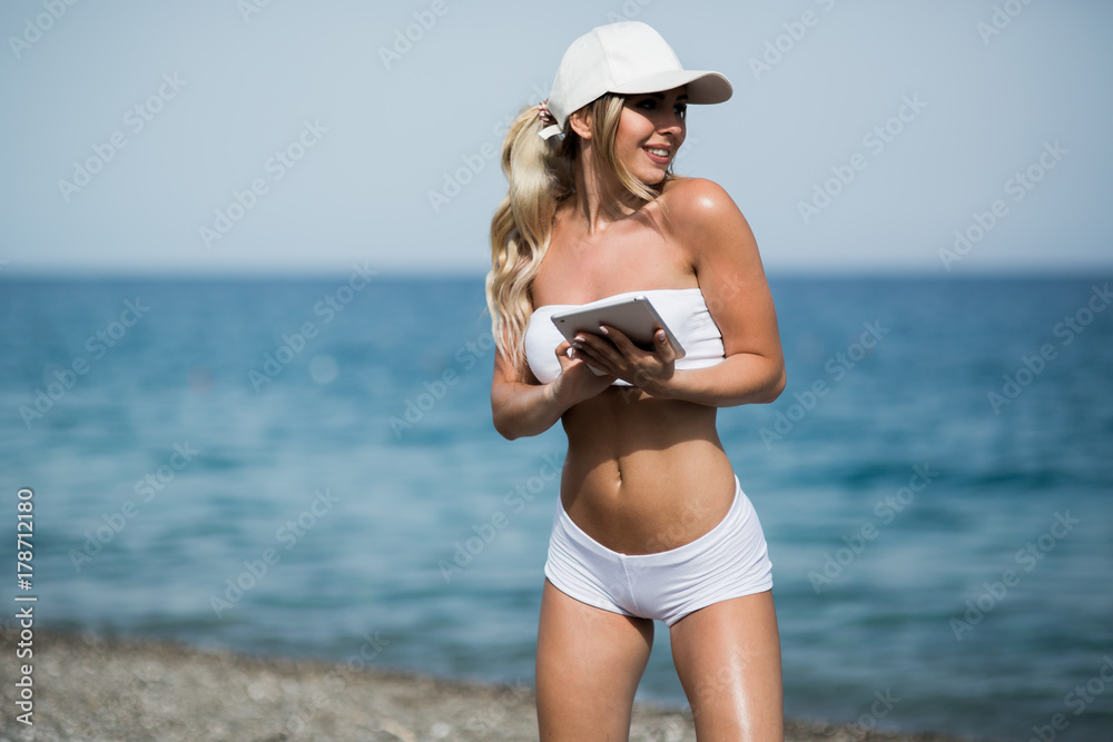 Young beautiful woman in sport suit is using her tablet on the beach