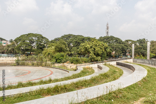 Ramp or cement steps or concrete steps with textured design and natural lawn formation. With group of trees in the background and huge pillars in the foreground.