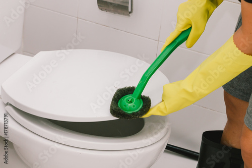 Housemaid wearing yellow rubber glove and using brush cleaning in the toilet