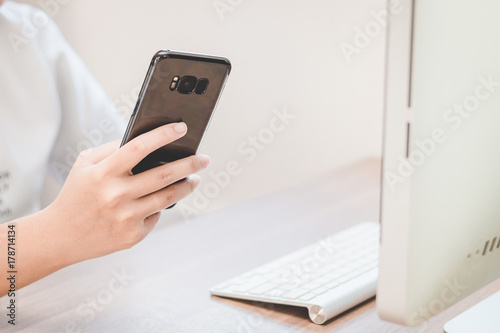 Hand holding black smart phone on back view in workspace