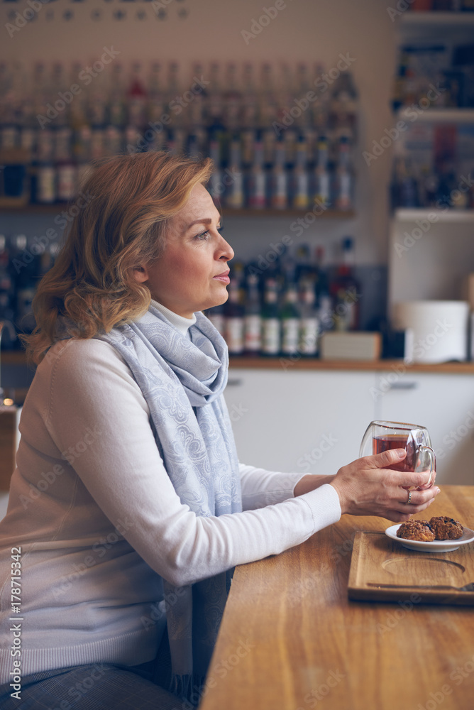 Dreaming mature woman with cup of tea sitting in cafe