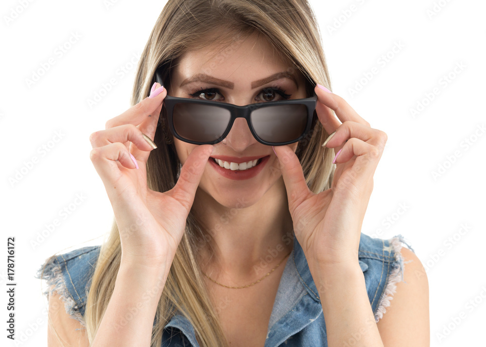 Friendly woman looks over the sunglasses. Blonde person wearing jeans vest. White background.. Friendly woman looks over the sunglasses. Blonde person wearing jeans vest. White background..