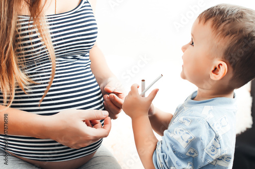 the child takes the cigarette from his pregnant mother photo