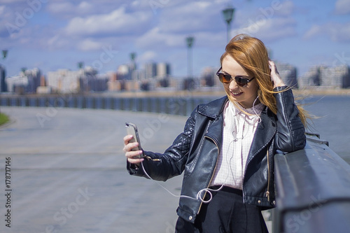 beautiful girl looks in the phone is photographed smiling on the street the sun shines