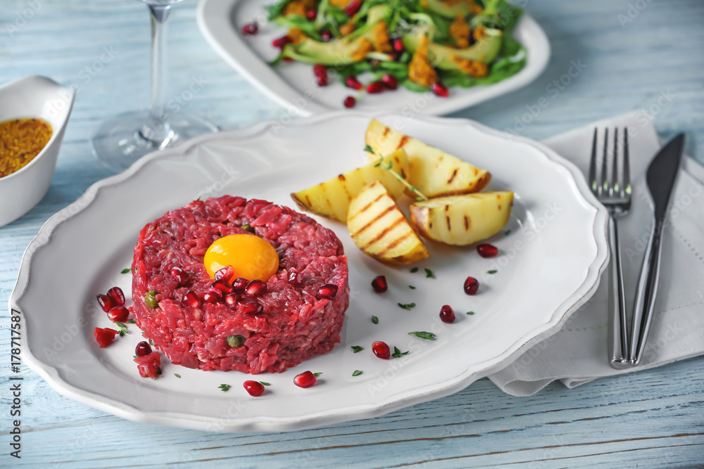 Delicious steak tartare with yolk, pomegranate seeds and potatoes on plate
