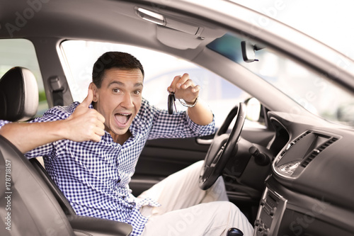 Happy man showing key and thumb up while sitting in new car