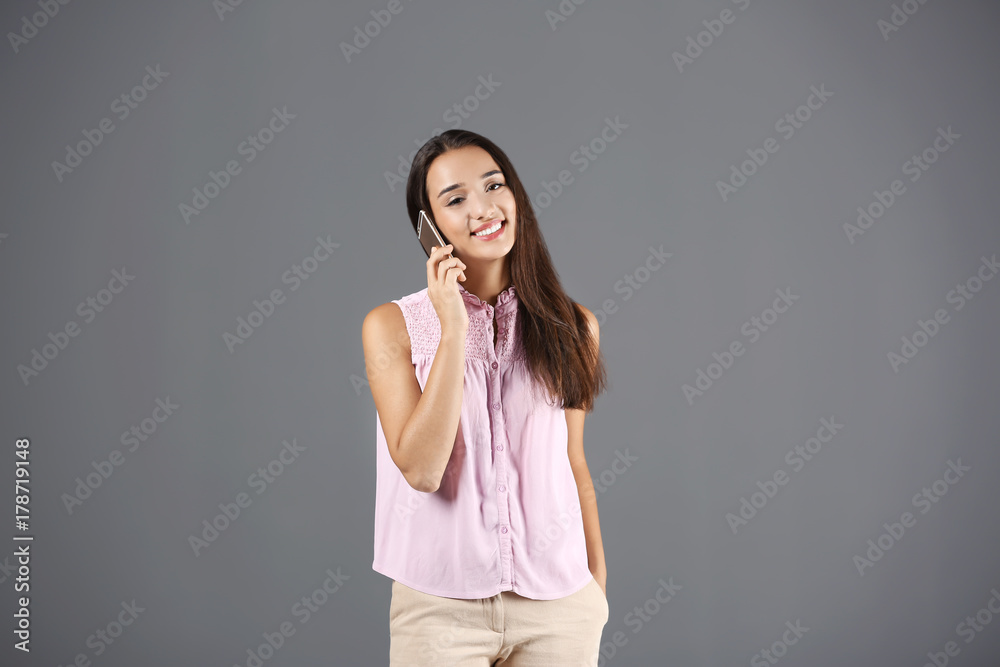 Beautiful young woman speaking by mobile phone on grey background Beautiful young woman speaking by mobile phone on grey background