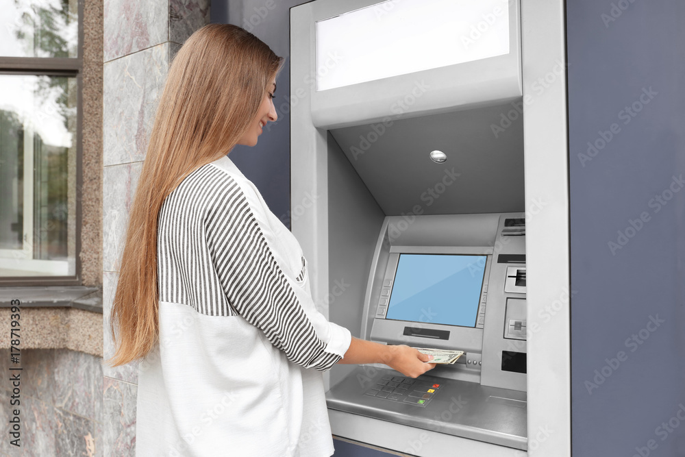 Fototapeta premium Woman taking money from cash machine outdoors