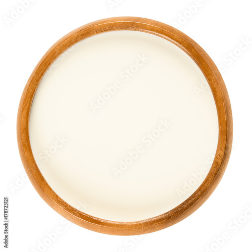 Fresh sweet cream in wooden bowl, a dairy product composed of the higher butterfat layer skimmed from the top of milk before homogenization. Macro food photo close up from above on white background.