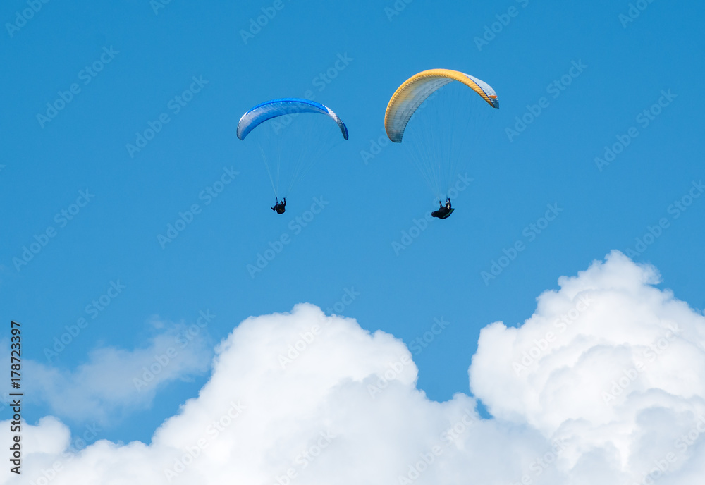 Two paragliders flying in the blue sky against the background of clouds. Paragliding in the sky on a sunny day. Two paragliders flying in the blue sky against the background of clouds. Paragliding in the sky on a sunny day.