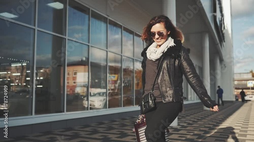 Woman in sun glasses a black leather jacket, black jeans with shopping bags, enjoying the walk in front of a mirrored store window on the street Steadicam shot