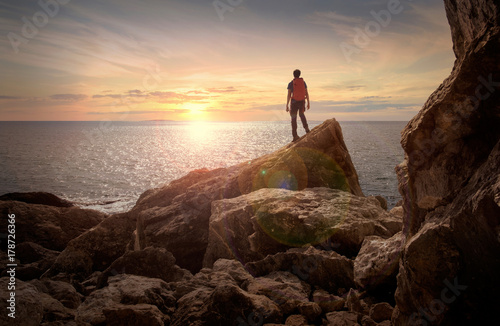 Sunset view. Man with backpack. Rocks at the sea ocean bank