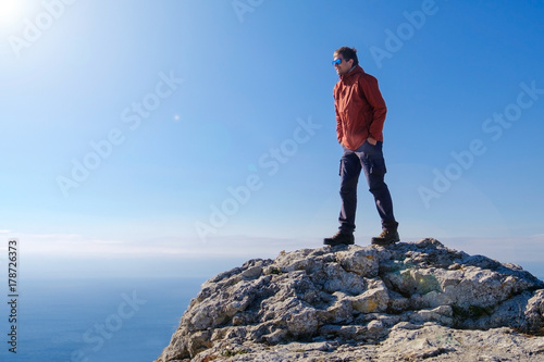 Smiling man in sunglasses standing at the peak of rock mountain. Daylight