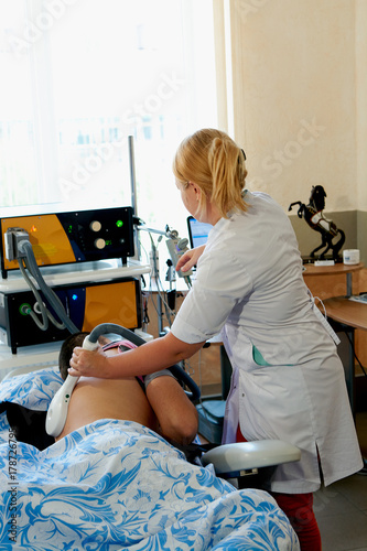 Female doctor does transcranial magnetic stimulation the man with a broken spine. Physiotherapy. Electrotherapeutic treatment of the back. photo