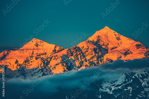 Evening view of sunset over the snowy mountain peak with misty clouds. Travel and nature background. Holiday, travel, sport, recreation. Kazbegi National Park, Gergeti, Georgia. Retro toning filter